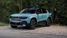 En blå elektrisk SUV som lades ved en ladestasjon i et grønt område.