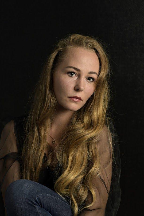 Portrett av en kvinne med langt, bølgete hår, iført en svart bluse, mot en mørk bakgrunn.