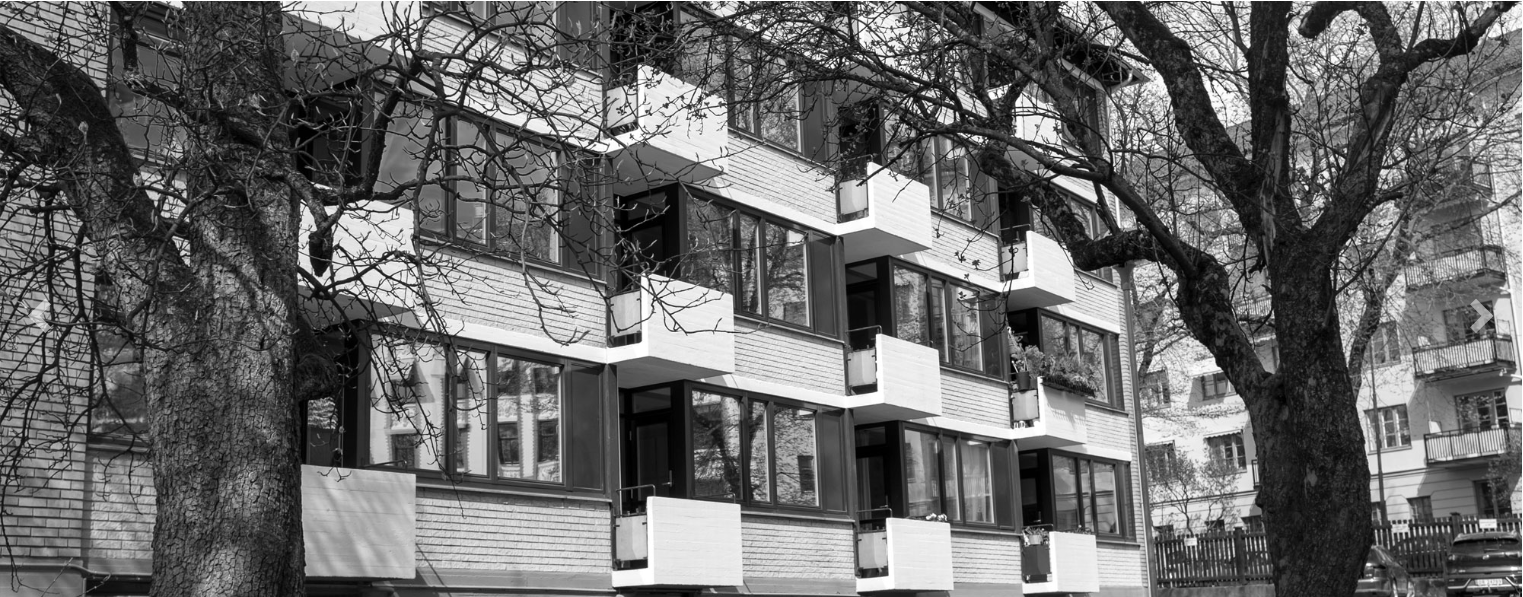 Moderne leilighetsbygg med store vinduer og balkonger, omgitt av trær i svart-hvitt.