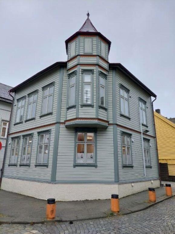 Et gammelt, grått trehus med tårn og mange vinduer, plassert på et hjørne i en gate.