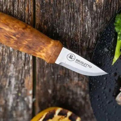 En Brusletto kniv med trehåndtak ligger på et bord med grønnsaker og mat.