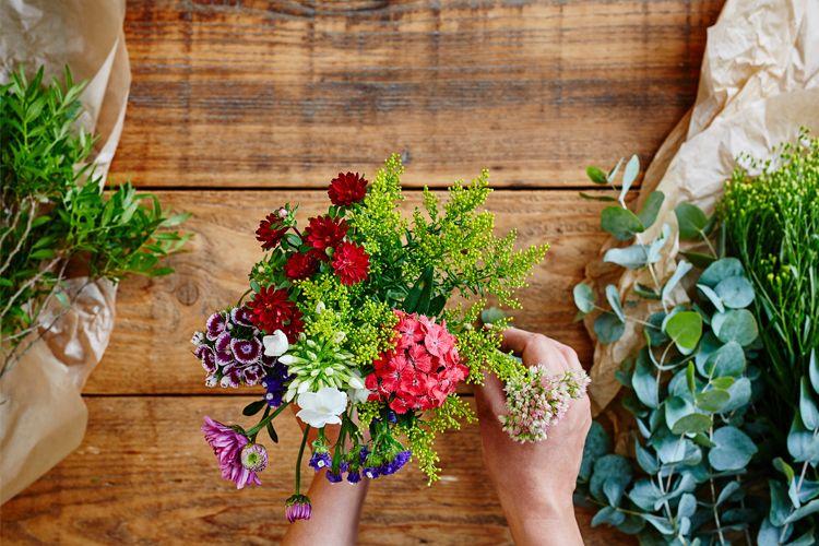 En person holder en fargerik blomsterbukett med forskjellige blomster på et trebord.