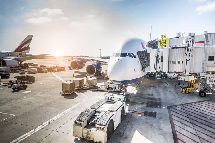 Et fly står ved en gate på flyplassen, med bagasje og servicekjøretøy i nærheten. Solen skinner i bakgrunnen.