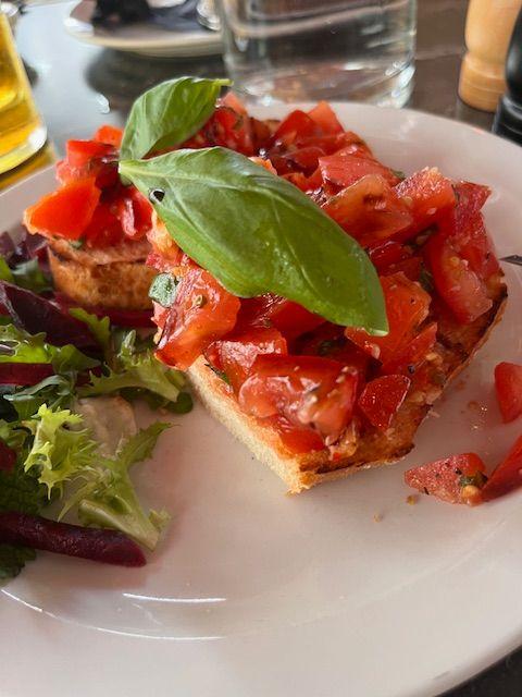 Bruschetta med tomater og basilikum servert med en frisk salat på en hvit tallerken.