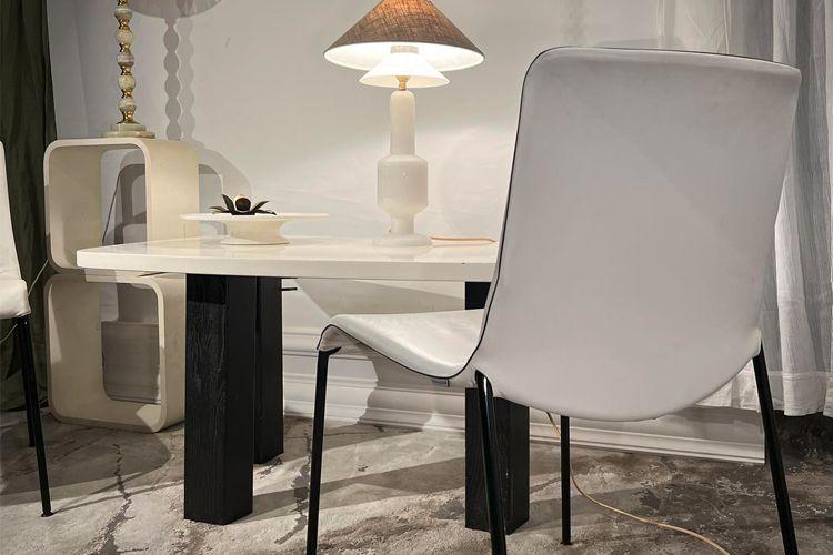 Moderne spisebord med hvit overflate, sorte ben og en stilren stol ved siden av en lampe.