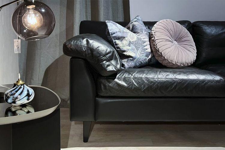 Moderne stue med en svart skinnsofa, dekorative puter og en stilren lampe ved siden av et rundt bord.