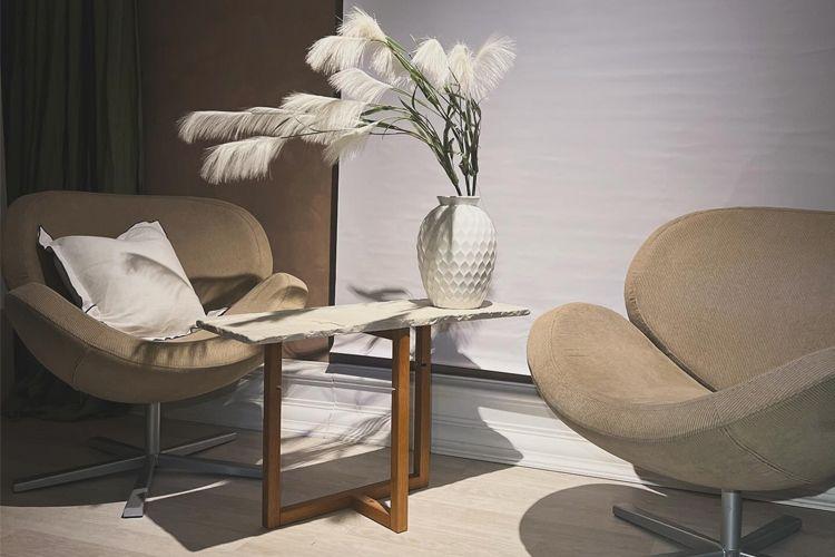 Moderne stue med to beige stoler, et marmorbord og en vase med dekorative planter.