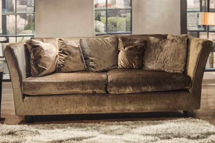 En brun sofa med flere puter, plassert på et teppe i et rom med store vinduer.