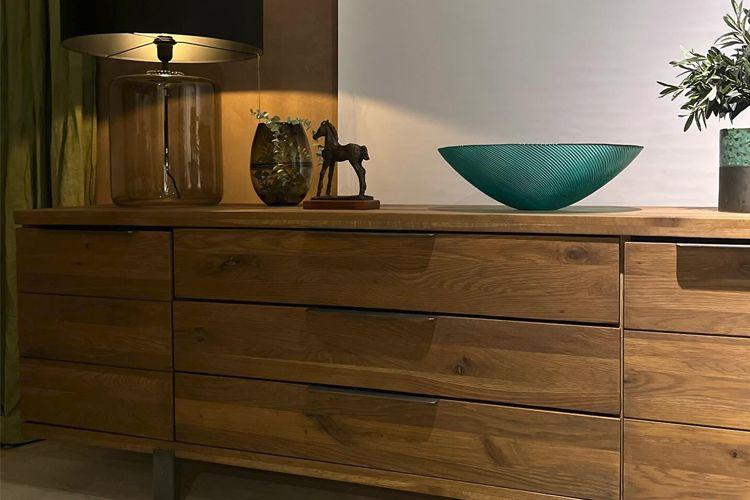 En moderne kommode i eik med seks skuffer, en lampe, en glassbolle og en dekorativ hestefigur.