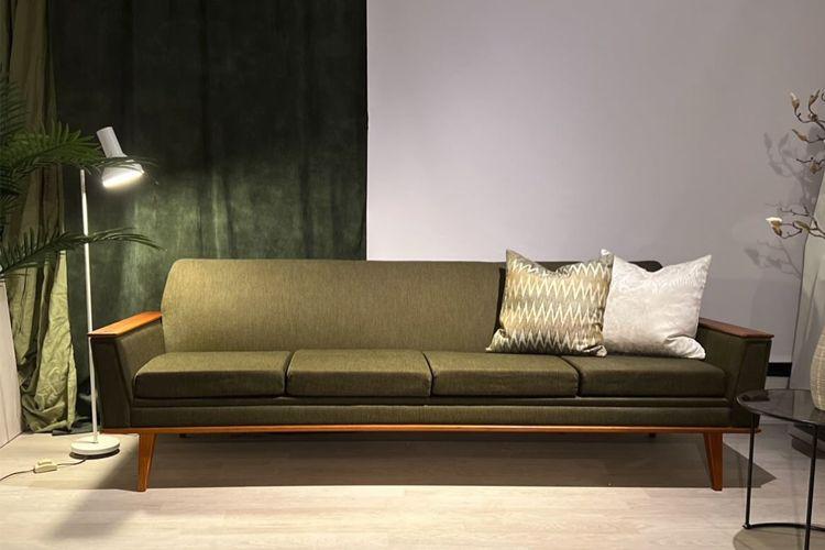 En moderne grønn sofa med treben og puter i forskjellige farger, plassert i et stilrent rom.