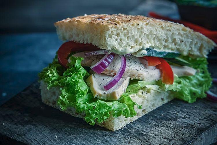 En fersk sandwich med kylling, salat, tomat og rødløk mellom to skiver brød.