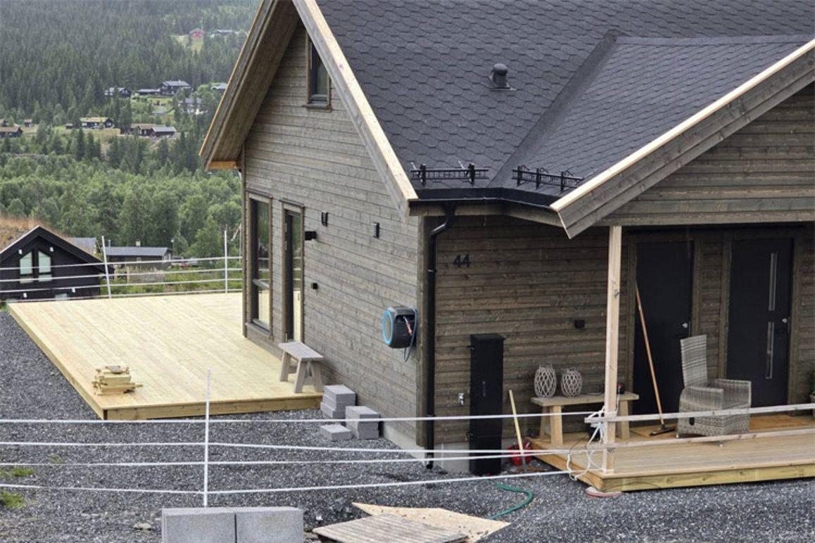 Moderne hytte med trepanel, terrasse og utsikt over landskapet, under bygging i naturskjønt område.