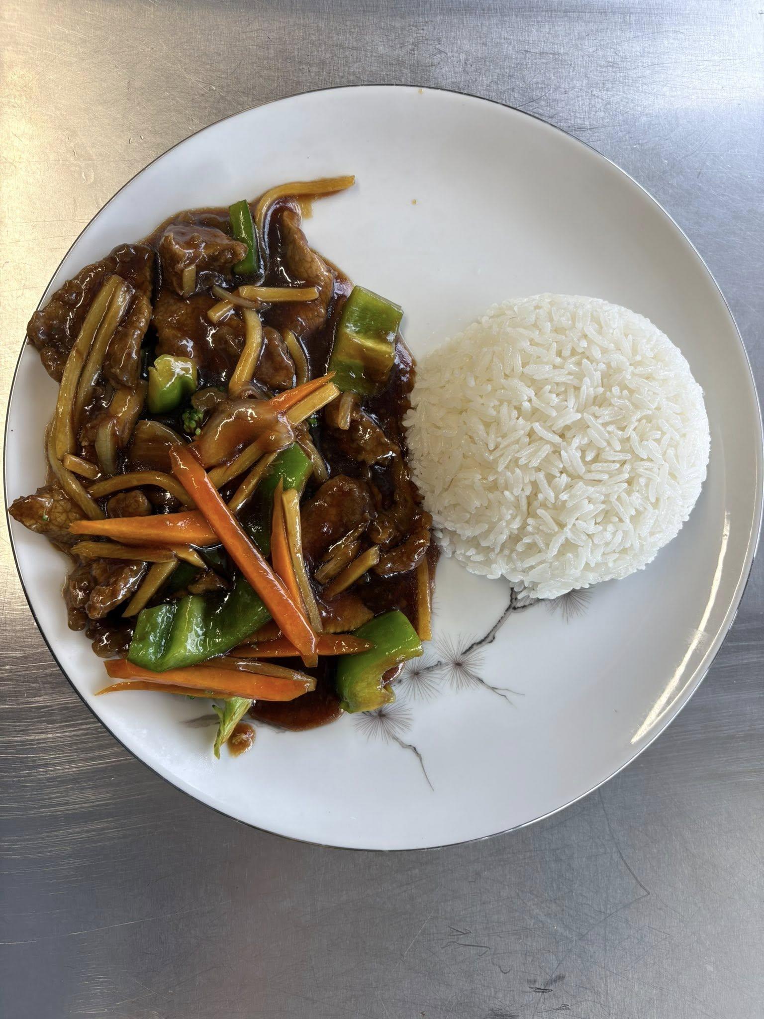 En tallerken med ris og woket biff med grønnsaker som gulrøtter og paprika i soyasaus.