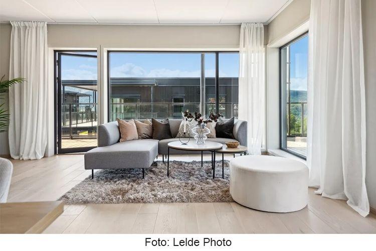 Moderne stue med grå sofa, runde bord og store vinduer som slipper inn naturlig lys.