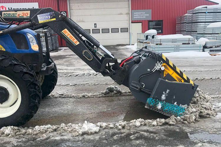 Traktor med snøfreser som fjerner snø fra en vei i vinterlandskap.