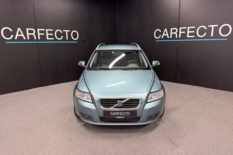 Blå Volvo stasjonsvogn foran en svart bakgrunn med teksten "CARFECTO" på veggen.
