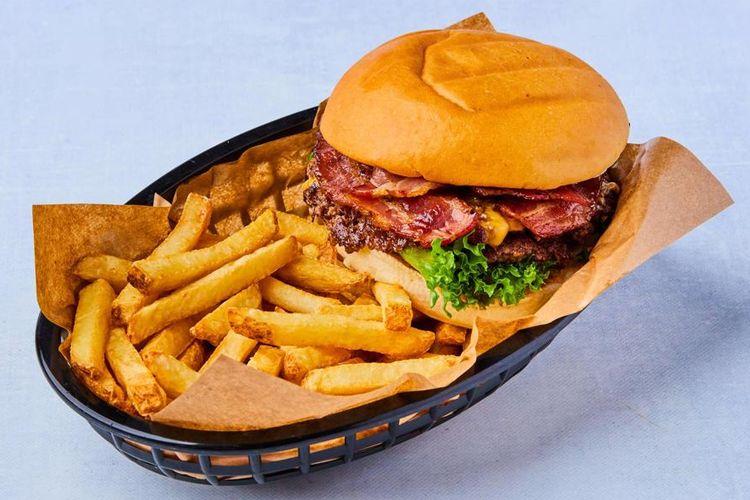 En saftig hamburger med bacon og salat, servert med sprø pommes frites i en kurv.