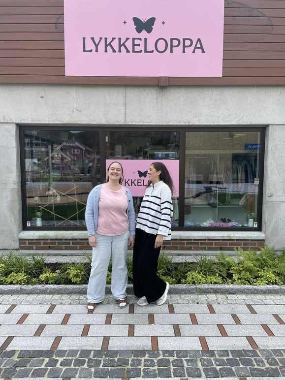 To kvinner står foran butikken Lykkeloppa med en rosa skilt og vinduer.