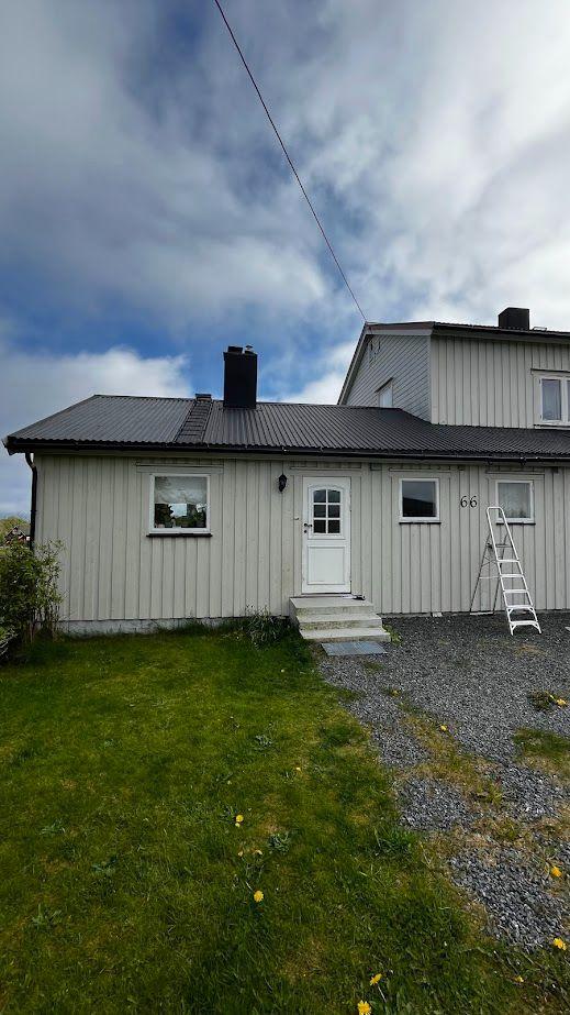 En hvit enebolig med grått tak, plassert på en gressplen med grusvei og stige ved siden av.