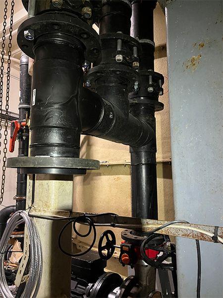 Rørledninger og ventiler i et teknisk rom, med svart plast og metallkomponenter synlige.