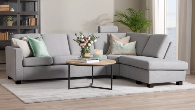 Moderne grå sofa med puter, blomsterdekorasjon og bord i stue med naturlig lys.