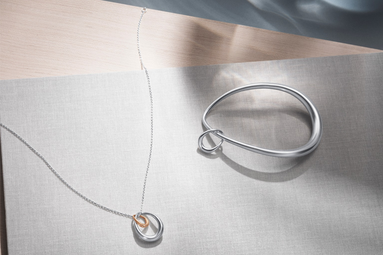 Sølv smykke med ring og kjede på en lys overflate, med reflekterende detaljer og moderne design.