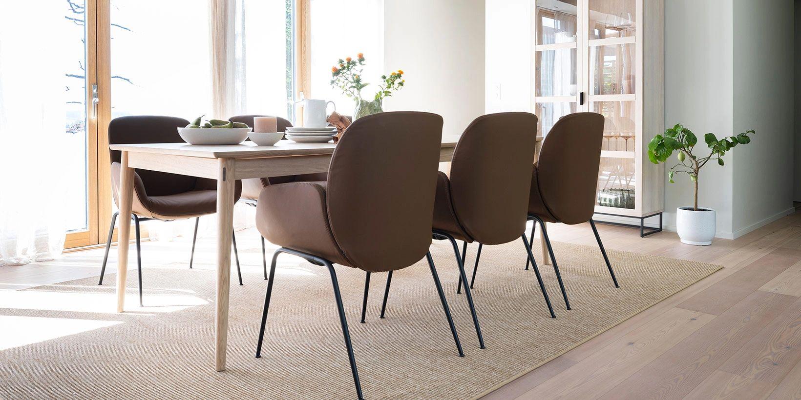 Moderne spisestue med et trebord, brune stoler og en lys teppe, omgitt av store vinduer.