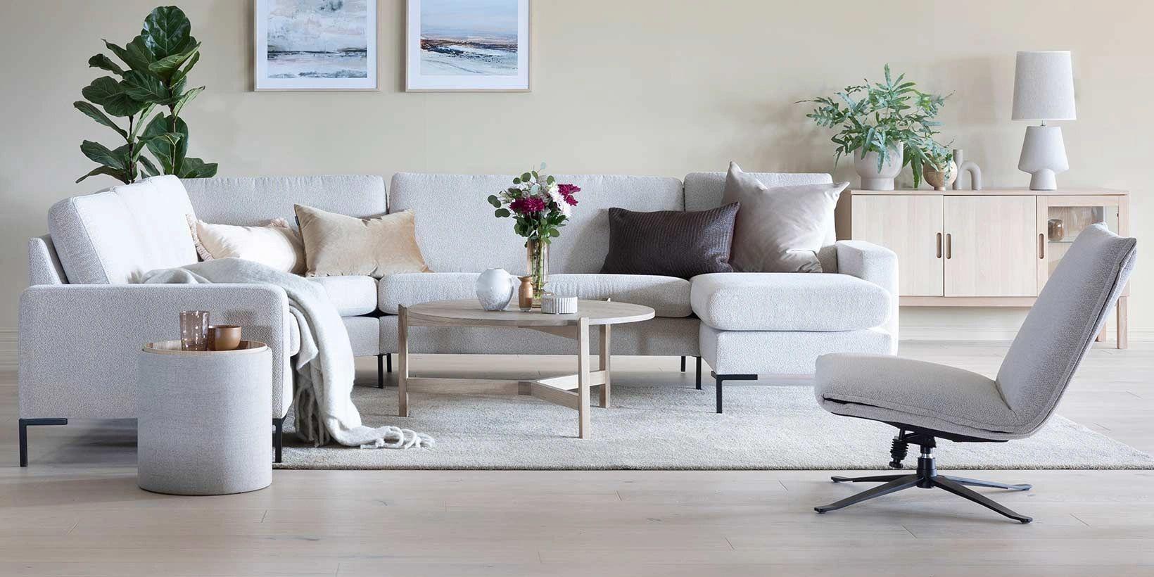Moderne stue med lys sofa, bord, planter og dekorative bilder på veggen. Komfortabel stol i forgrunnen.
