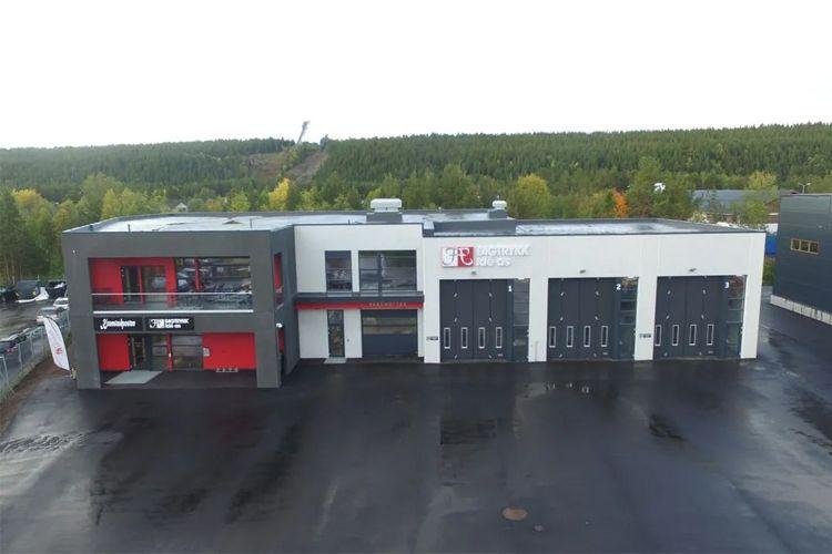 Moderne næringsbygg med lagerporter og kontor, omgitt av skog og asfaltparkering.