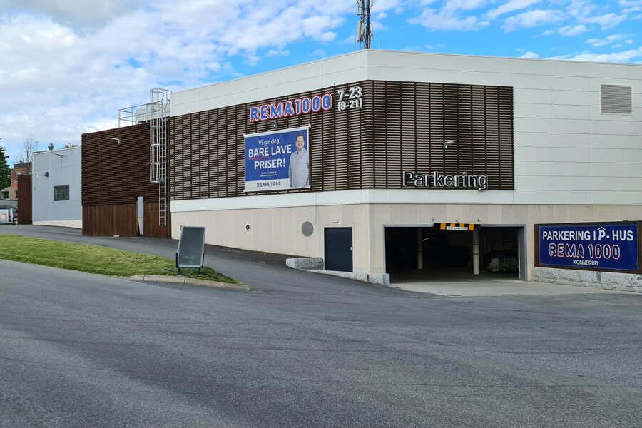 En moderne bygning med parkering, skilt med "REMA 1000" og "Åpent" i nærheten av en vei.