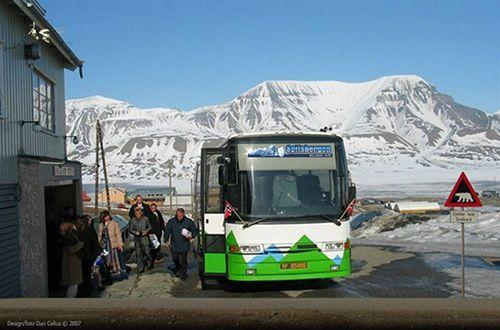En buss med grønn og hvit farge står ved en bygning, mens passasjerer går av i et snødekt fjellandskap.