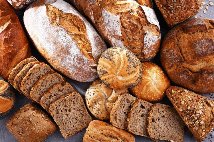 Et utvalg av ferskt brød, inkludert rundstykker, loff og grovt brød, pent arrangert på en overflate.