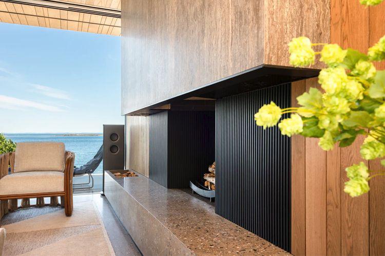 Moderne peis med svart panel og stein, med utsikt over havet og en komfortabel stol i rommet.