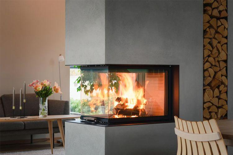 Moderne peis med flammer i et stilrent stueinteriør, blomster og vedstabel i bakgrunnen.