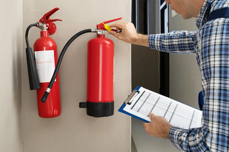En person sjekker brannslukkere på veggen med en sjekkliste i hånden.