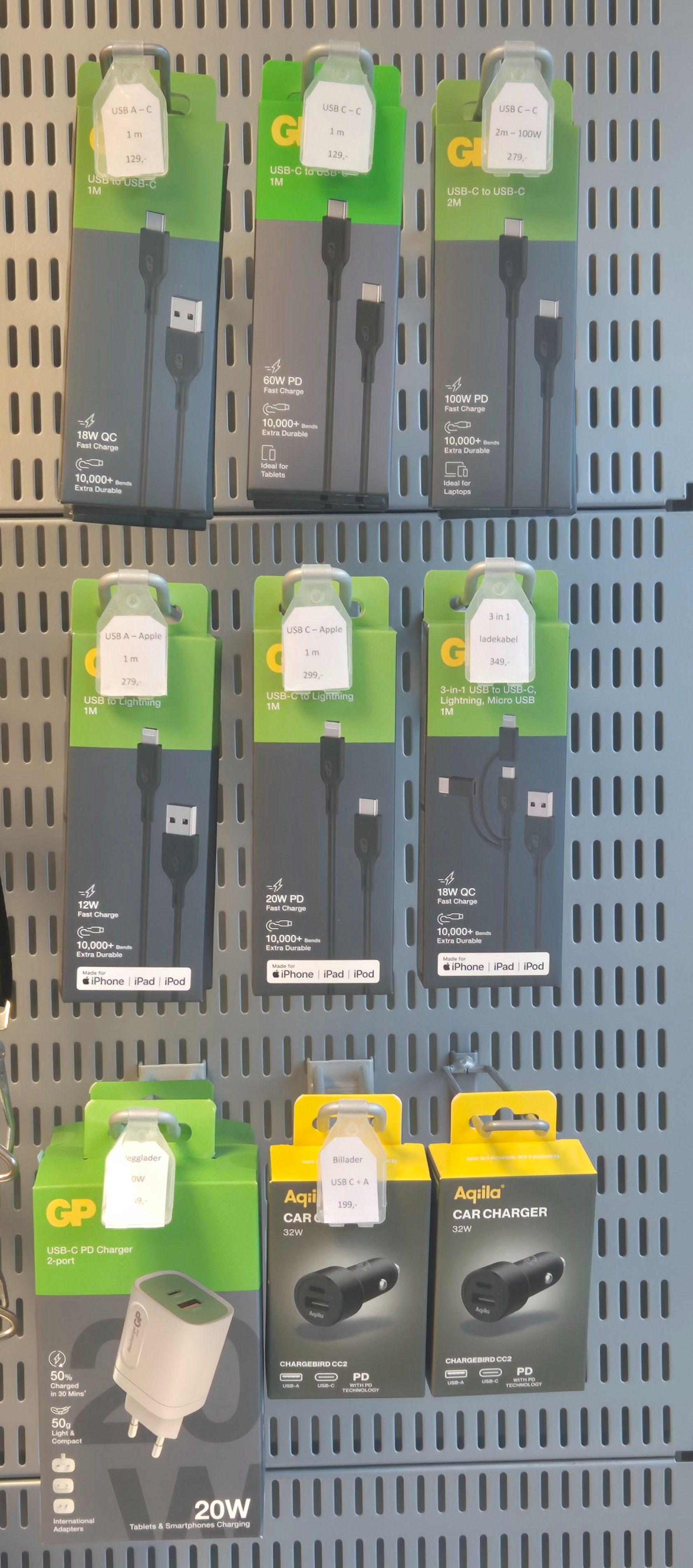 Batteriladere og USB-kabler i emballasje på en butikkhylle, med ulike modeller og spesifikasjoner.