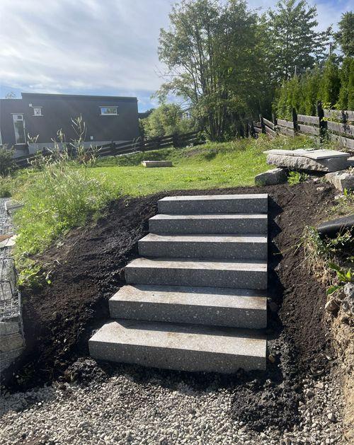 Grå granitttrapper som fører opp til en hage med grønt gress og trær i bakgrunnen.