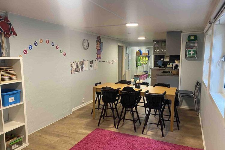 Moderne stue med spisebord, stoler, og kjøkken i bakgrunnen, dekorert med bilder og fargerike detaljer.