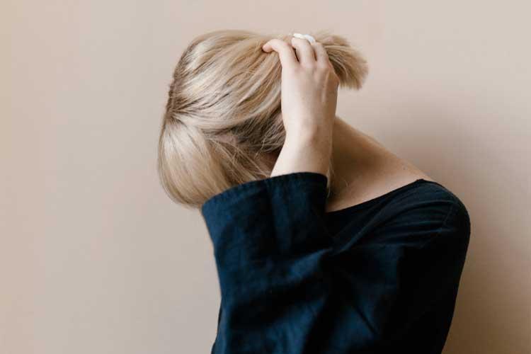 En kvinne med blondt hår som holder håret bakover, iført en svart genser mot en lys bakgrunn.
