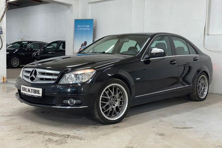En svart Mercedes-Benz C-klasse sedan med aluminiumsfelger står i en bilutstillingshall.