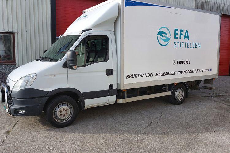 En hvit lastebil med EFA-stiftelsen logo parkert foran en lagerbygning.
