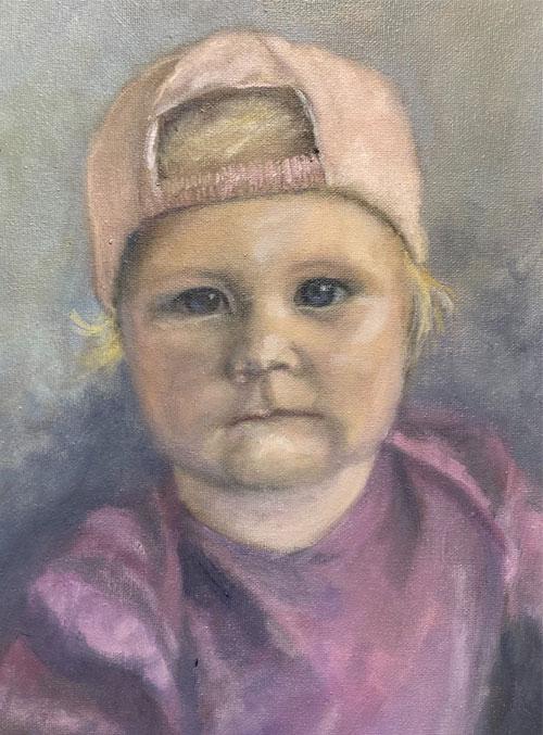 Portrett av et lite barn med blondt hår og rosa caps, iført en lilla t-skjorte.