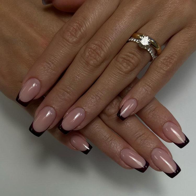 Hender med lange negler i nude farge med svart fransk manikyr og en ring med diamant.