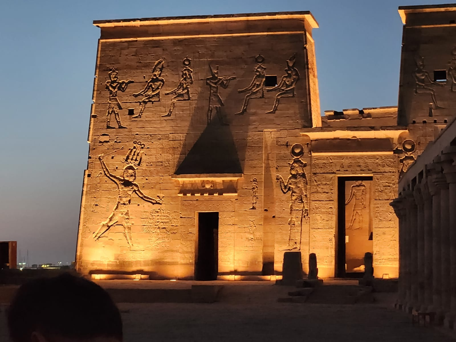 Et opplyst egyptisk tempel med hieroglyfer og statuer, sett ved skumring.