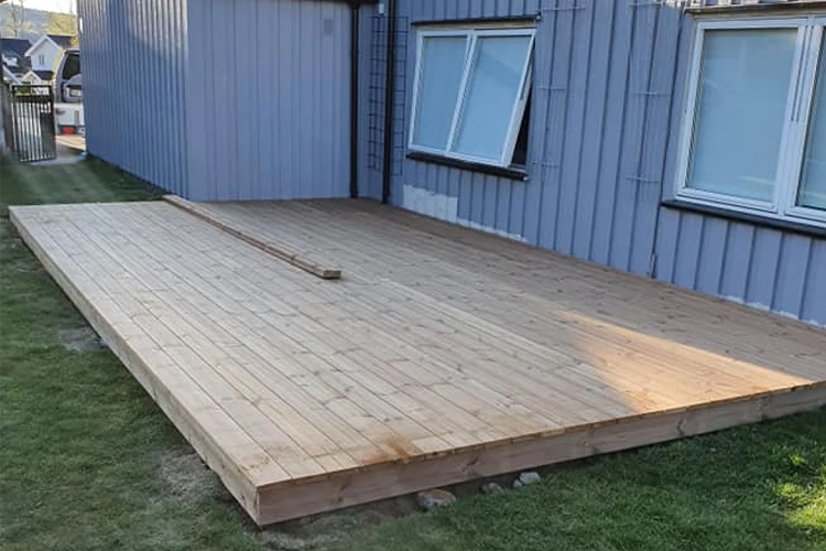 Trekonstruksjon av en terrasse i tre ved siden av en bygning med vinduer.