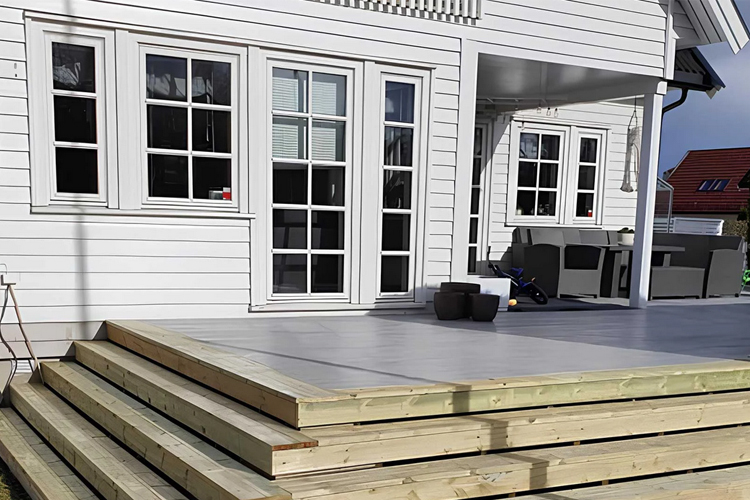 Moderne hus med hvit fasade, store vinduer og en treterrasse i forgrunnen.