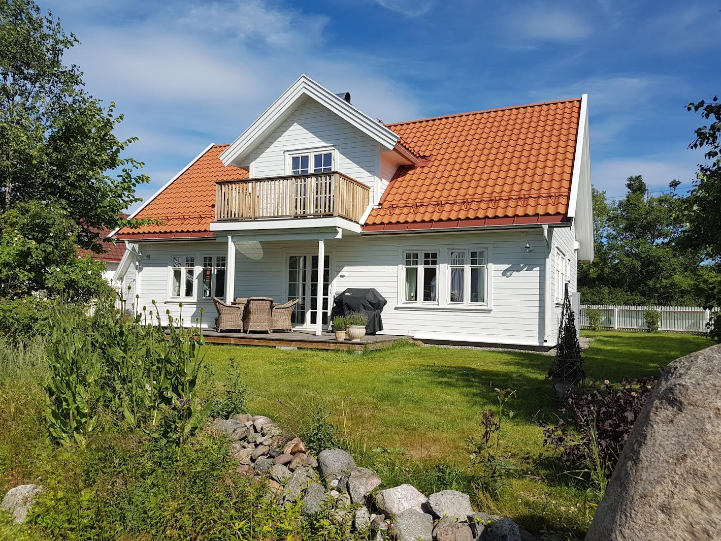 En vakker, hvit enebolig med rød takstein og balkong, omringet av grønt gress og trær.