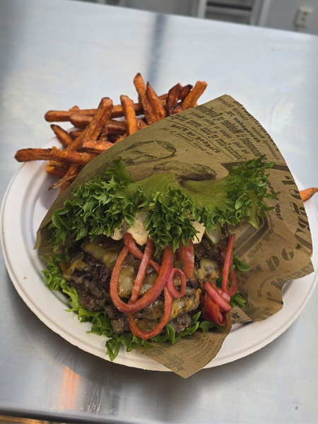 Saftig hamburger med ost, salat, løk og dressing, servert med sprø søtpotetfries på en tallerken.