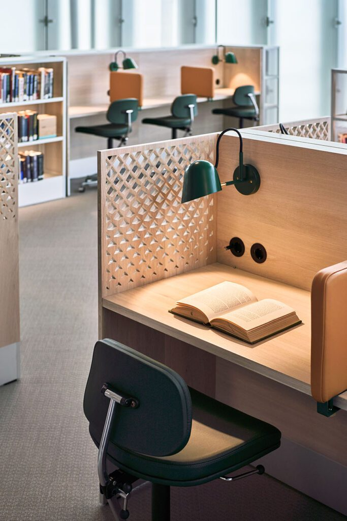 Moderne studiebord med en åpen bok, stoler og bokhyller i et lyst rom.