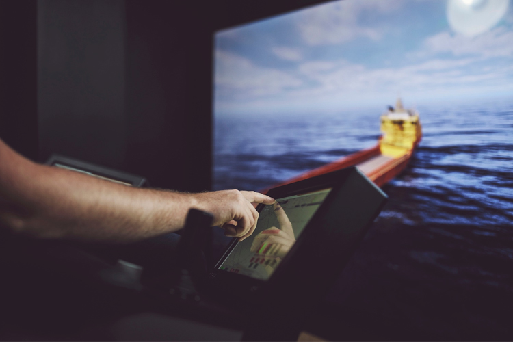 En person som peker på en skjerm med en simulering av et fraktskip på havet.